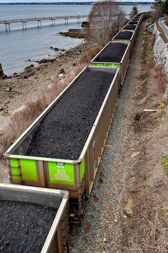 A coal train passes along the Bellingham waterfront between a popular hotel/spa and the Taylor Street Dock.