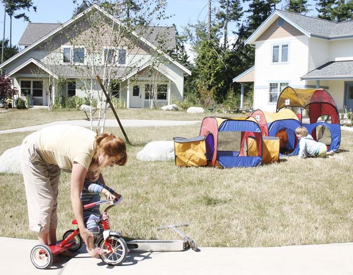 Nomi Ross helps her 1-year-old son Jasper sit on a tricycle in the courtyard in front of their new home in the San Juan Community Home Trust’s affordable home neighborhood
