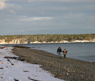 An unidentified couple walks along a beach at Cattle Pass this afternoon. A brisk breeze was blowing. The woman is holding a small dog under each arm.