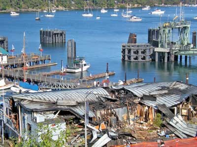 Boats and blue water bob in the background of the charred remains of the Friday Harbor waterfront building destroyed by fire Saturday