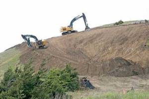 Construction crews rely on heavy equipment and earth movers to carve out a corridor and build a reinforcement berm on Mount Finlayson in the early phase of realignment and relocation of Cattle Point Road