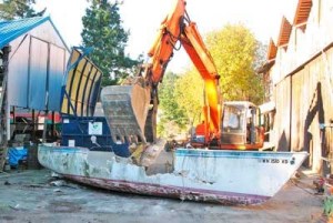 Heavy equipment assists in the dismantling of a fiberglass sailboat at Deer Harbor Boat Works