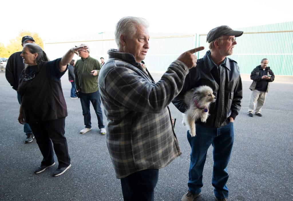 John Norman (center) explains which way pilot Ron Fowler, holding his dog, will take Normans replica of the Spirit of St. Louis out for its first flight at Arlington Municipal Airport on July 28. Heather Norman (left) explains the same to a friend. (Andy Bronson / The Herald)