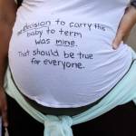 A pregnant protester is pictured with a message on her shirt in support of abortion rights during a march, Friday, June 24, 2022, in Seattle. The U.S. Supreme Court's decision to end constitutional protections for abortion has cleared the way for states to impose bans and restrictions on abortion — and will set off a series of legal battles. (AP Photo/Stephen Brashear)