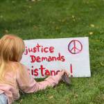 An island youth lies in the grass with her sign as she listens to the speakers.